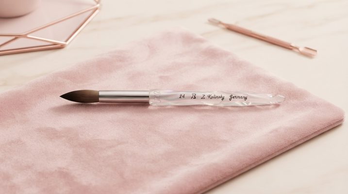 A pristine Kolinsky nail brush artfully displayed on a blush pink velvet surface, embodying elegant salon styling.